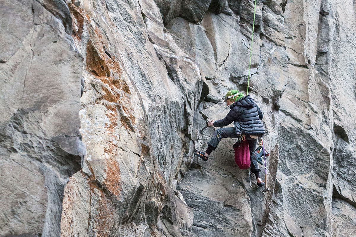 Das Bild zeigt einen Kletterer beim Ausbouldern der züge in einer neuen Route. An einer grau-braunen Felswand hängt der Kletterer im rechten Bildteil im Seil und versucht einen Kletterzug. Er trägt eine schwarze JAcke und Mütze weil es windig und kalt ist.