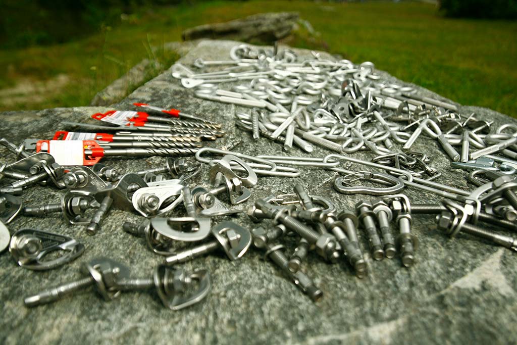 Das Bild zeigt Einbohrartikel für den Bergführer Pro Deal von bolting.eu. Auf einer Felsplatte liegen verschiedene Einbohr Hardware aus silber glänzendem Stahl wie Bohrhaken, Bohrhakenlaschen, Bohrer und Klebehaken.