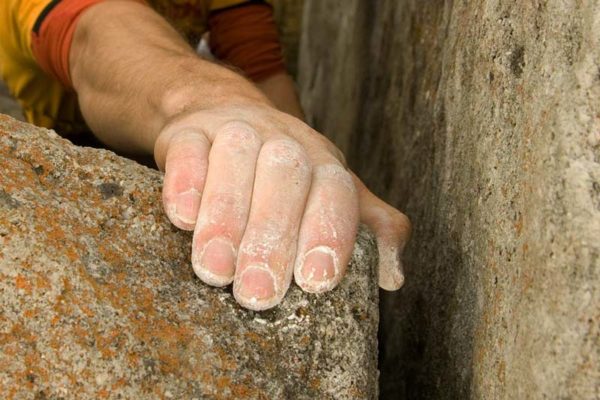 Das Bild zeigt eine Hand eines Kletterers auf einem Felsblock mit Chalk zum Klettern an den Fingern.