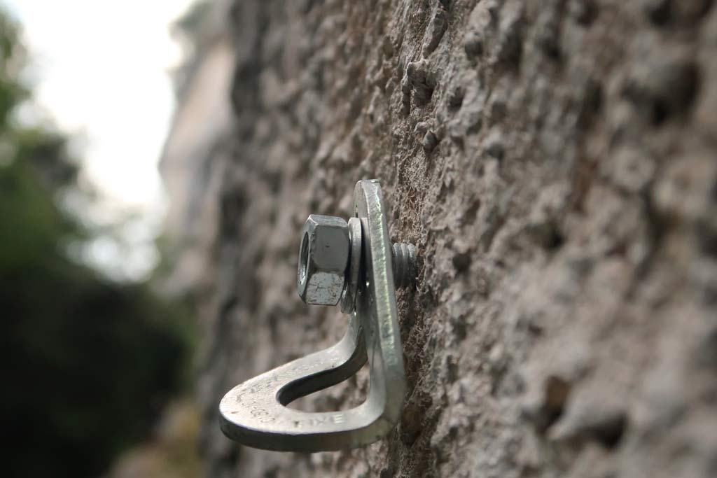Das Bild zeigt einen Bohrhaken mit lockerer Laschein einer grauen Felswand. Das Bild soll die Problemlatik von lockeren Laschen in Klettergärten verdeutlichen.