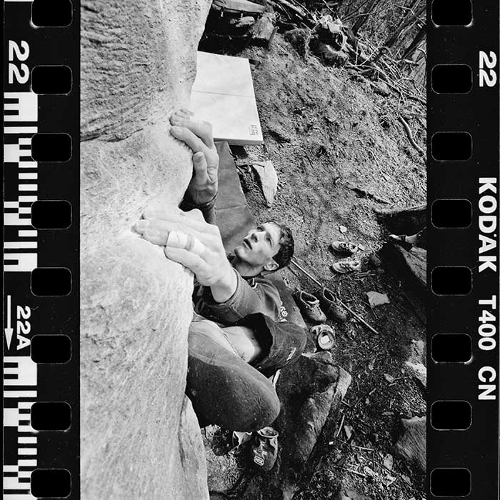 Das Bild zeigt einen gescannten Schwarz-Weiss Film mit einem Boulderer darauf. Im Hintergrund liegen ein paar Bouldermatten am Boden.