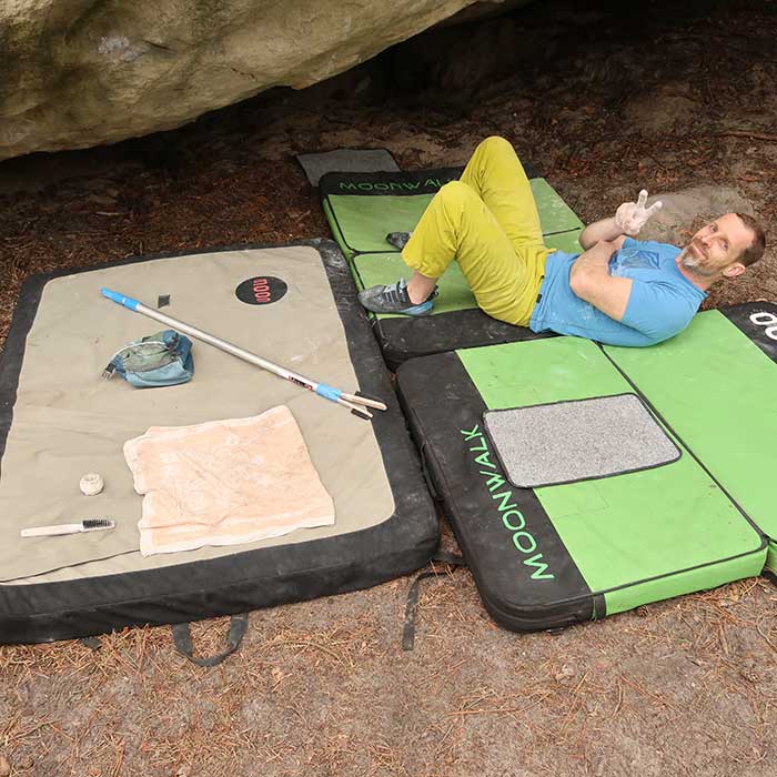 Das Bild zeigt einen lächelnden Boulderer auf einer MAtte mit Boulder Zubehör bei seinen Beinen.