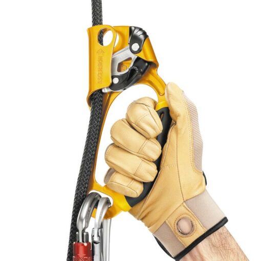 Das Bild zeigt die gelbe Petzl Ascension Handsteigklemme mit einer Hand in Lederhandschuhen am Griff.