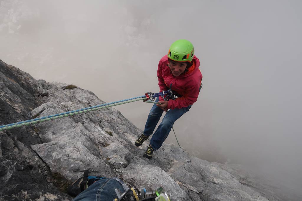 Das Bild zeigt eine Klettererin beim Abseilen in Schlechtwetter mit einem Kurzprusik.