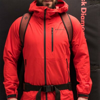 Das Bild zeigt einen Kletterer mit roter Jacke der eine Bouldermatte mit einem Tragegurt bzw. Hüftgurt am Rücken hat.
