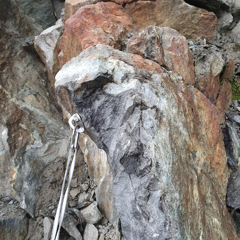 Das Bild zeigt einen Bohrhaken in einem großen Felsblock der aber leider in einem Bereich mit extrem losen GEstein steckt. Es soll die falsche Anbringung eines Fixpunktes zeigen.