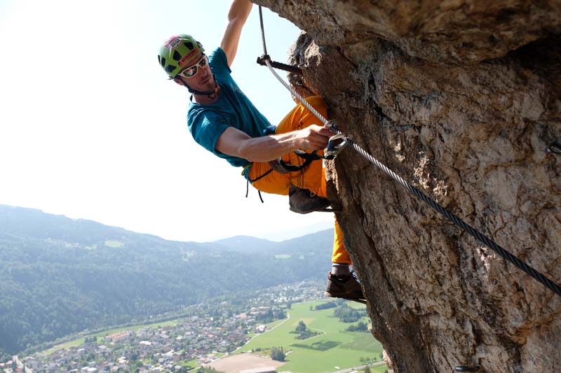 Das Bild zeigt einen Kletterer beim Umhängen seines Klettersteigset an einer überhängenden Stelle.