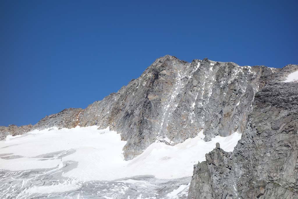 Das Bild zeigt die Südseite der Hochalmspitze mit Felswänden und Gletscherrest bei blauem Himmel.
