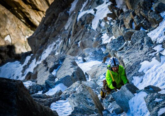 Das Bild zeigt einen Alpinisten in einer hochalpinen Wand beim Eisklettern mit eisgeräten.