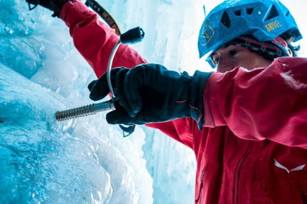 Eiskletterer mit roter Jacke beim Eindrehen einer Grivel 360 Eisschraube.