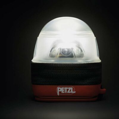 Petzl Noctilight Schutzetui mit eingeschalteter Lampe darin leuchtet als Laterne vor dunklem Hintergrund.