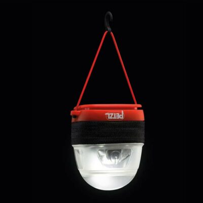 Petzl Noctilight Schutzbox mit eingeschalteter LAmpe darin aufgehängt als Laterne vor dunklem Hintergrund.
