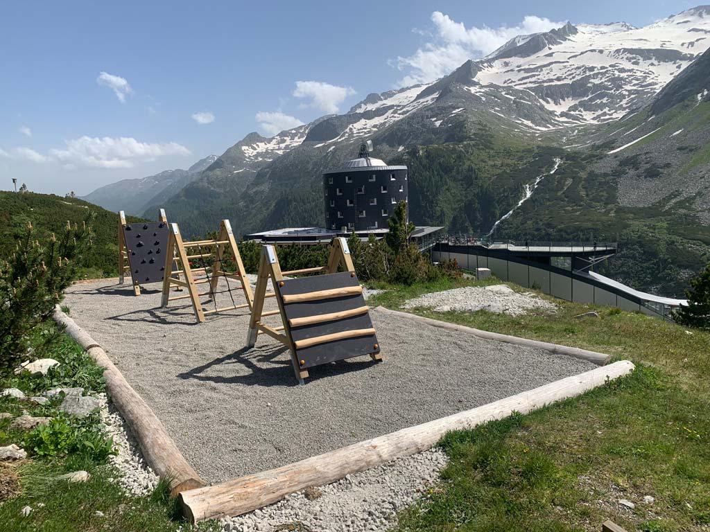 Sprossenböcke über Kiesbett am Abenteuerweg Kölnbrein mit Berghotel Malta und Bergen im Hintergrund.