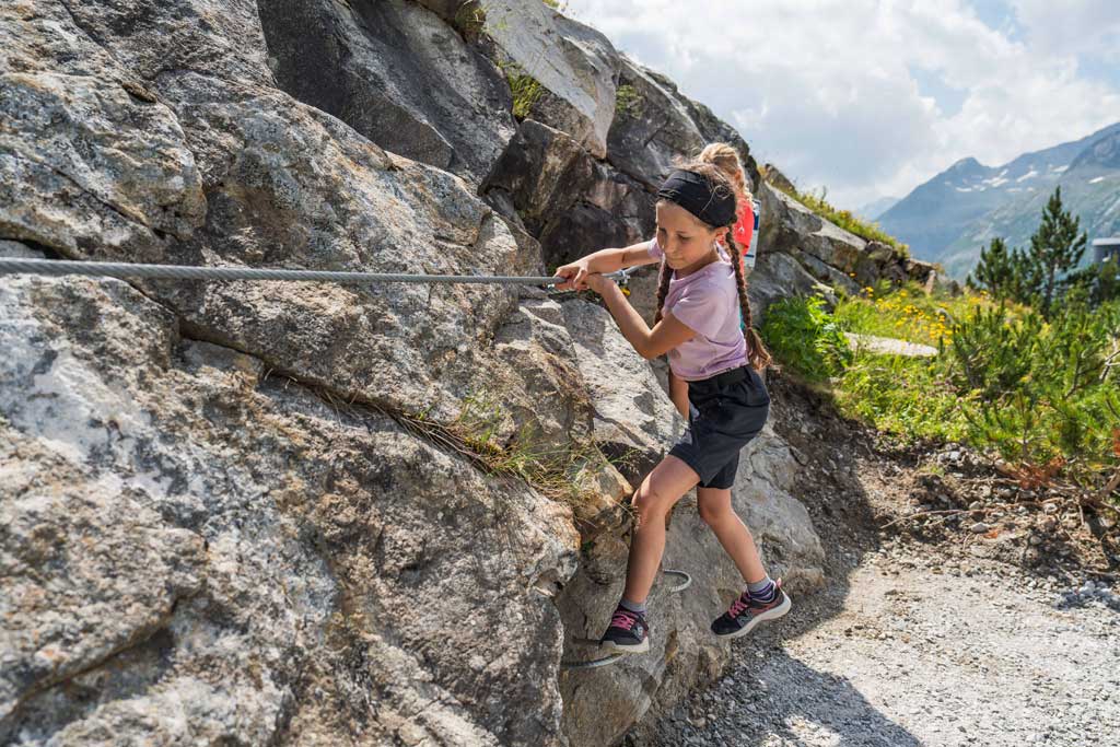 Mädchen auf einem Kinderklettersteig des Abenteuerweg Kölnbrein, sie hält sich an einem Drahtseil fest.