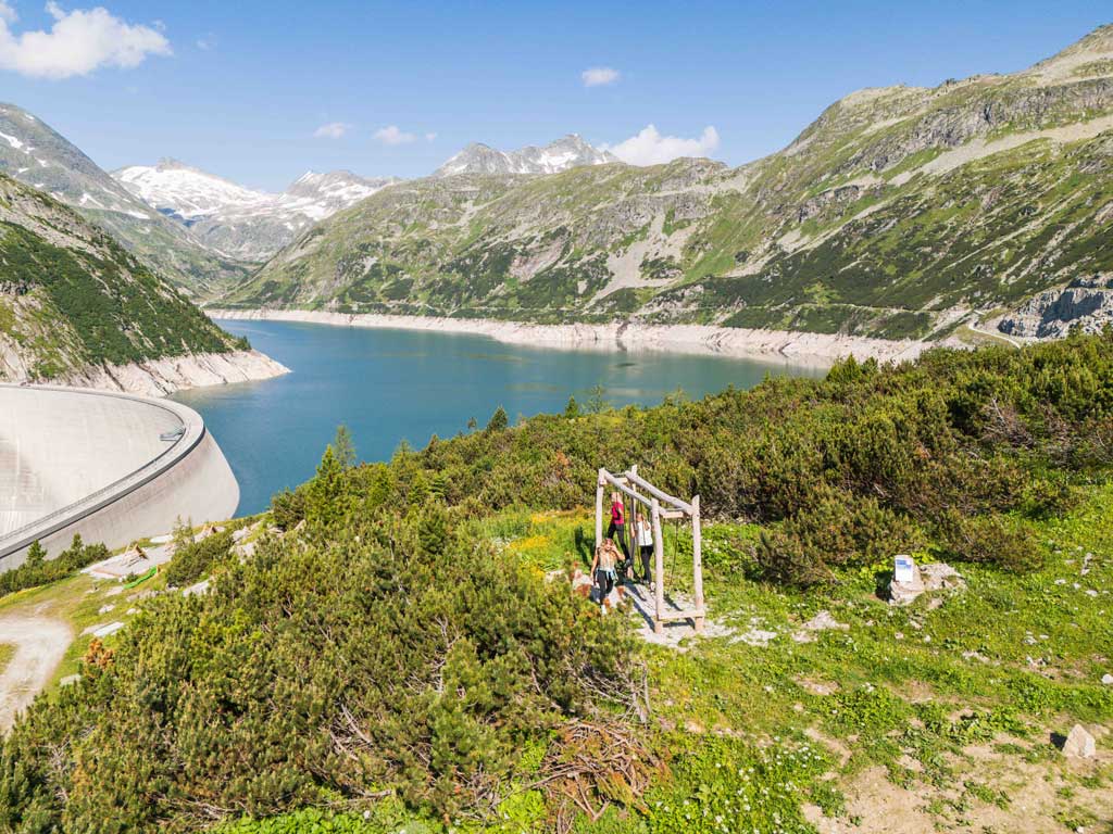 Kinder auf einer der Stationen des Abenteuerweg Kölnbrein in alpiner Landschaft und mit Stausee im Hintergrund.