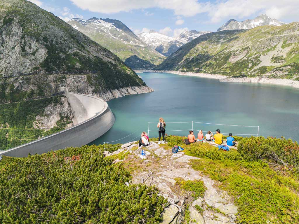 Familie die am Aussichtspunkt kuppe des Abenteuerweg Kölnbrein rastet. Unter ihnen die Kölnbreinsperre und der Stausee.