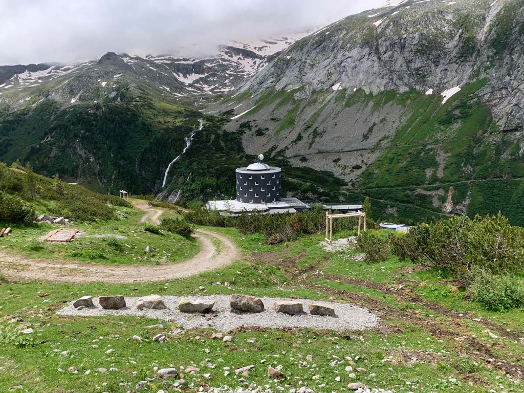 Linie mit großen Steinen am Abenteuerweg Kölnbrein mit Hotel und BErgen im Hintergrund.