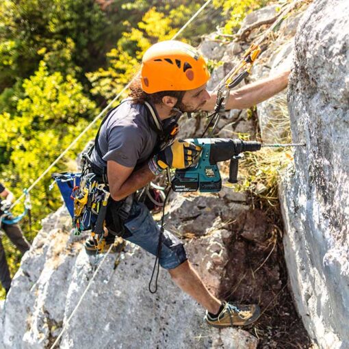 Kletterer mit orangem Helm und Bohrmaschine bei einem Einbohrkurs - Hakensetzerkurs in Bosnien von bolting.eu