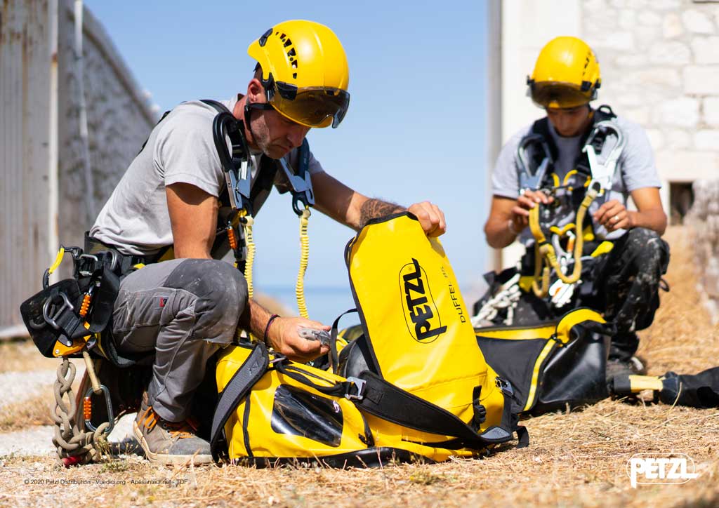 Zwei Industriekletterer mit gelben Helmen und Petzl Transportsäcken am Boden.