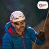 Kletterer mit Helm und blauer Jacke sowie Kletterbrille für Brillenträger vor einer Sonnenbrille.