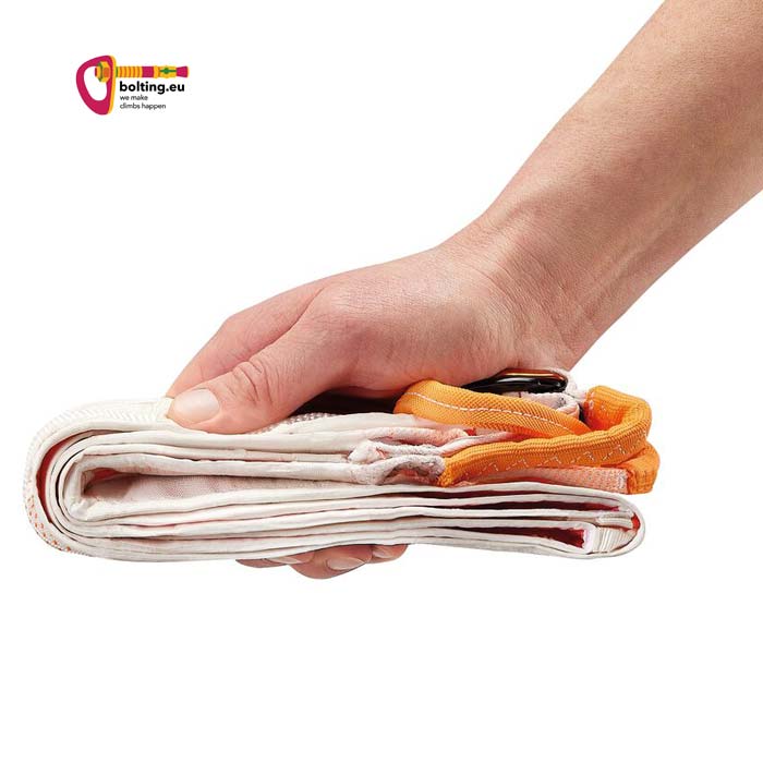 Eine Hand hält einen gefalteten Petzl Whisper Klettergurt zwischen den Fingern um das kleine Packmaß zu zeigen..