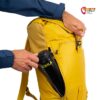 Hand steckt Trinkflasche in die seitliche Reißverschluss TAsche eines gelben Alpinist 22 Rucksackes von Kohla.
