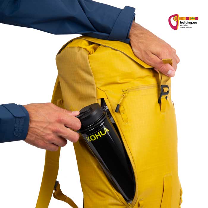 Hand steckt Trinkflasche in die seitliche Reißverschluss TAsche eines gelben Alpinist 22 Rucksackes von Kohla.