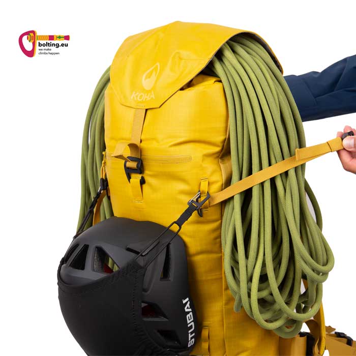 Hand zieht einen Riemen an Deckeltasche eines gelben Kletterrucksacks um Seil zu befestigen.