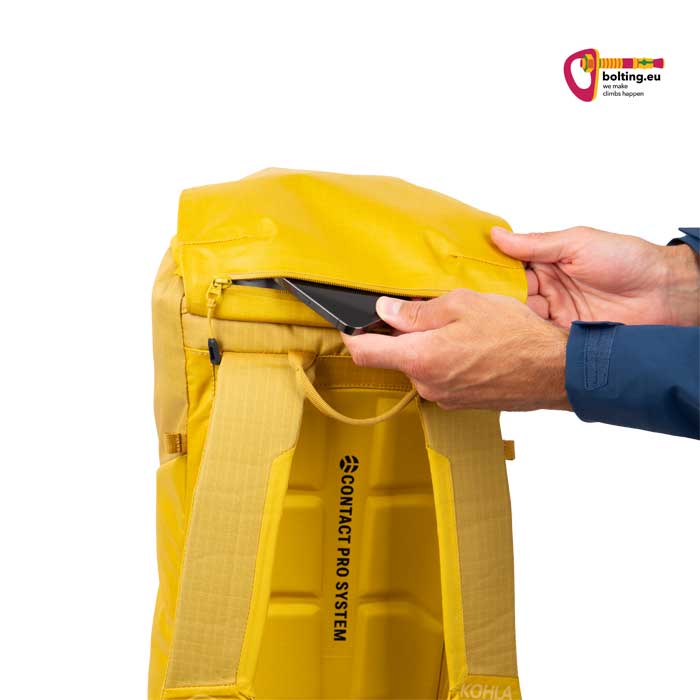 Hand steckt ein Handy in die Deckeltasche eines gelben Kletterrucksacks.