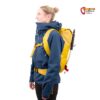 Modell in blauer Jacke mit gelbem Kohla Alpinist 22 Hochtourenrucksack und Eisgeräten von der Seite.