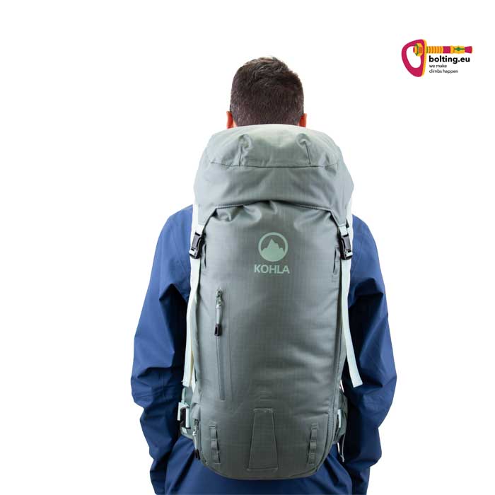 Lavendelfarbener Alpinrucksacks am Rücken eines Modell mit baluer Jacke.