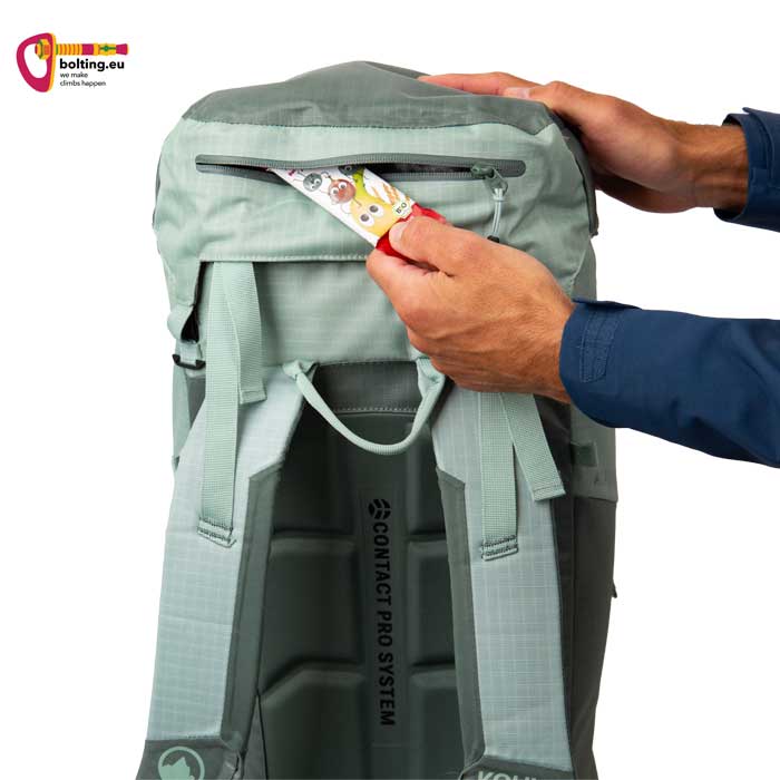 Hand steckt Müsliriegel in die Deckeltasche eines lavendelfarbenen Kohla Alpinrucksack.