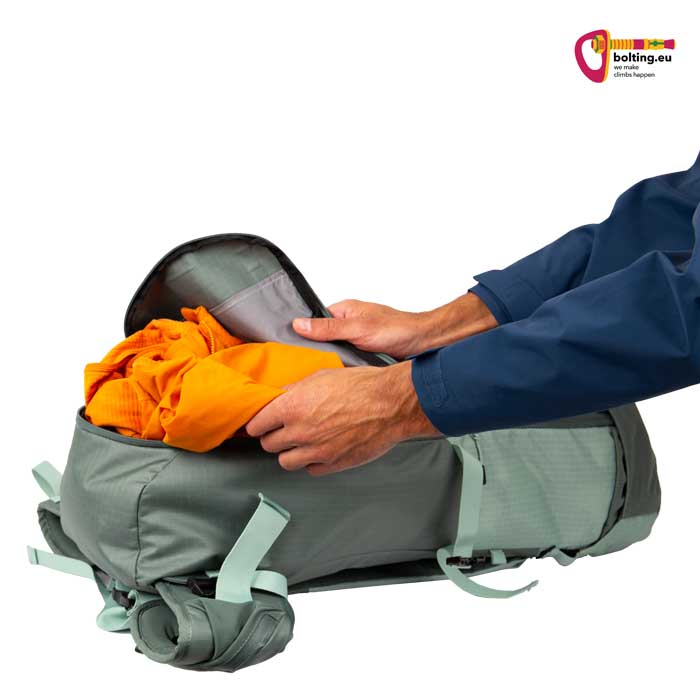 Hand steckt orangen Pulli in einen lavendelfarbenen Kohla Alpinrucksack.