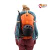 Modell mit orangem Alpinrucksack mit Seil und Helm.
