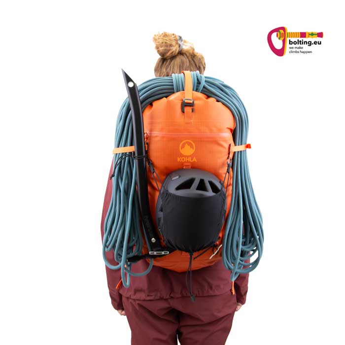 Modell mit orangem Alpinrucksack mit Seil und Helm.