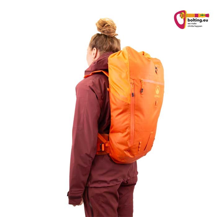 Modell mit lila Bekleidung und orangem Rucksack.