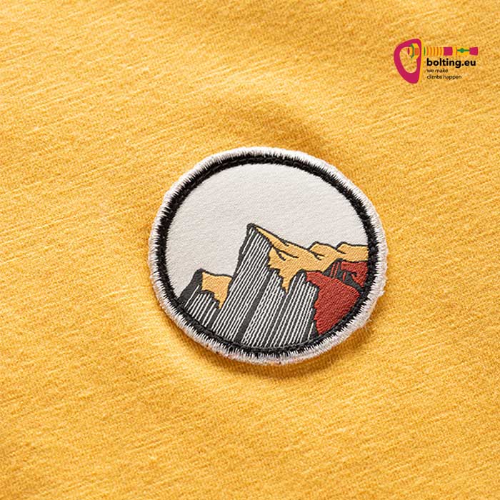 Detail eines orangen Herren Klettershirt mit rundem Berglogo.