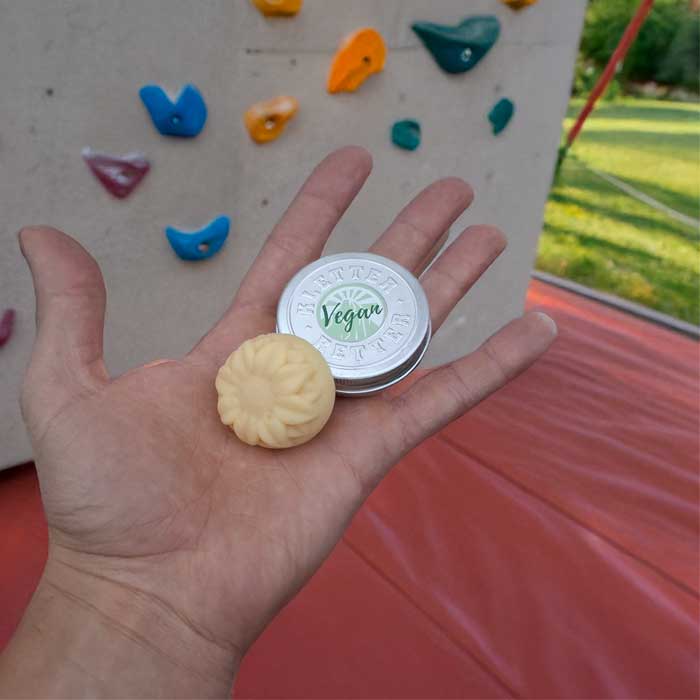 Eine Hand hält eine Dose KletterRetter vegane Skindisc vor einer Kletterwand.